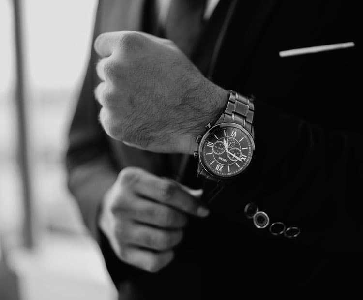 Black and white image of someone in a black suit is wearing a watch